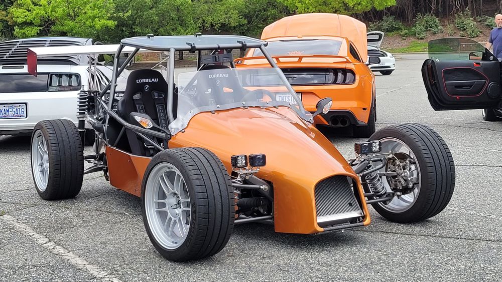 Metallic orange DF Goblin V1 at a car meet with windscreen, wide wheels, and rear wing, parked among sports cars.