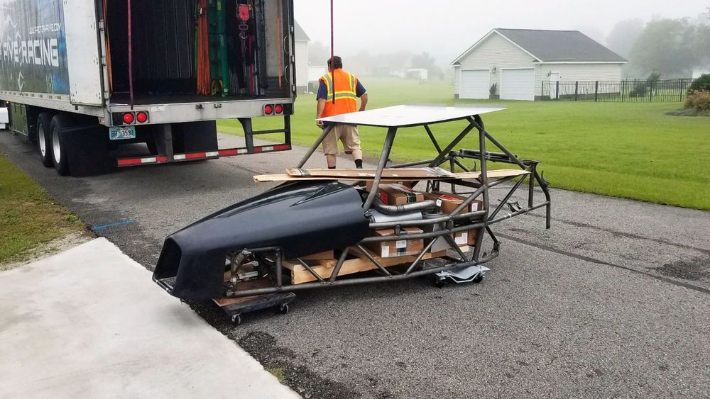 DF Goblin V1 kit delivery at curbside, bare chassis on a dolly with boxes and front body panel, being unloaded from a freight truck in a neighborhood.