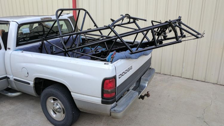 Goblin chassis loaded in the bed of a white Dodge pickup truck, resting on moving blankets with ratchet straps for protection during transport.