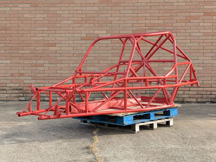 Goblin V2 chassis in Prismatic Washed Red powder coat, front quarter view, resting on shipping pallets against a brick wall.